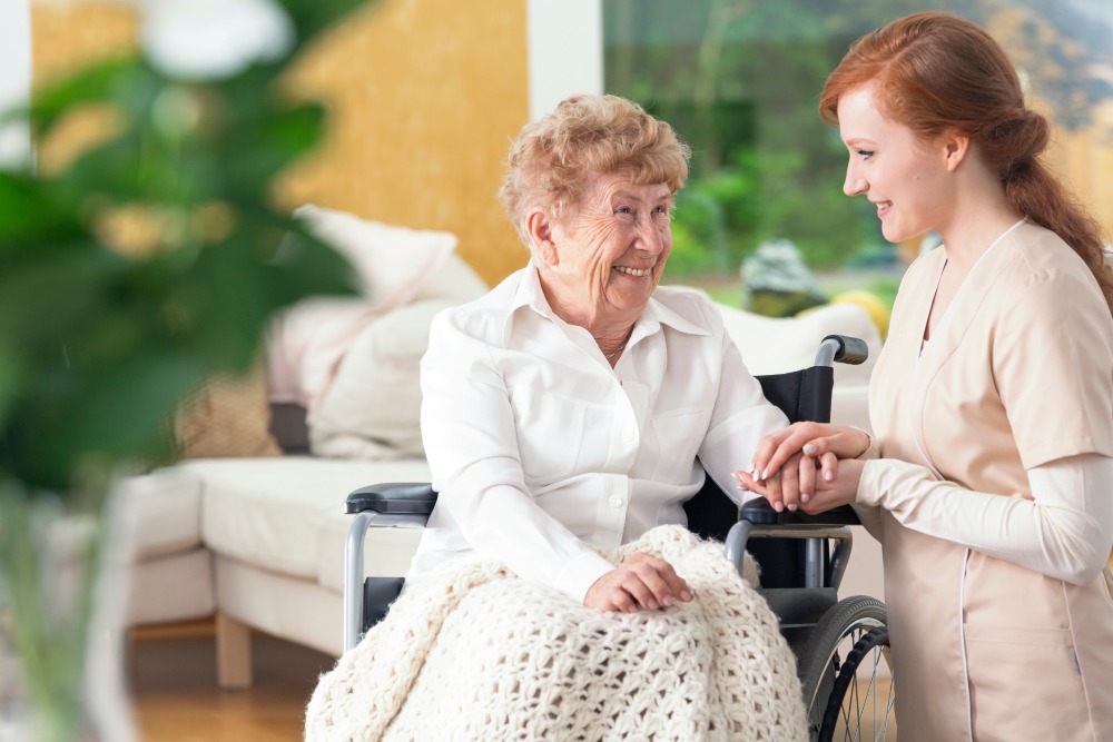 Smiling grandmother in a wheelchair and a friendly nurse talking and laughing